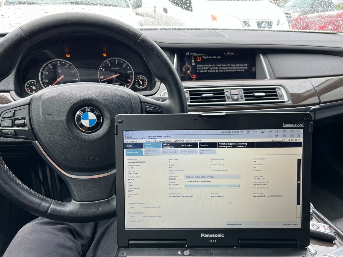 BMW 740i F01 interior with iDrive showing a TPMS warning, a Panasonic Toughbook CF-53 running BMW ISTA on the vehicle details tab