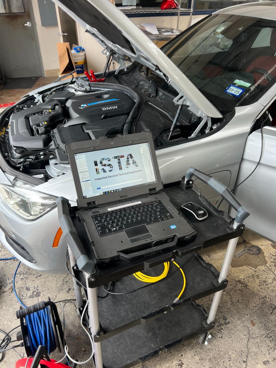 BMW with the hood up in the Spot-On programming bay, a Dell Latitude on a rolling cart running BMW ISTA (Integrated Service Technical Application)