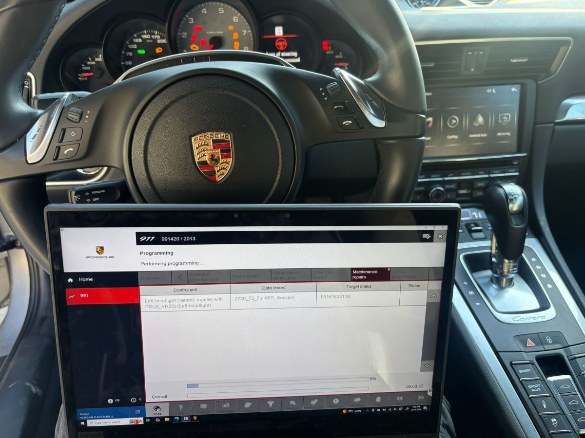 Porsche 911 991.2 Carrera interior with Porsche steering wheel, PIWIS programming a left headlight control unit (PDLS_VR06 master) shown on a connected Lenovo laptop