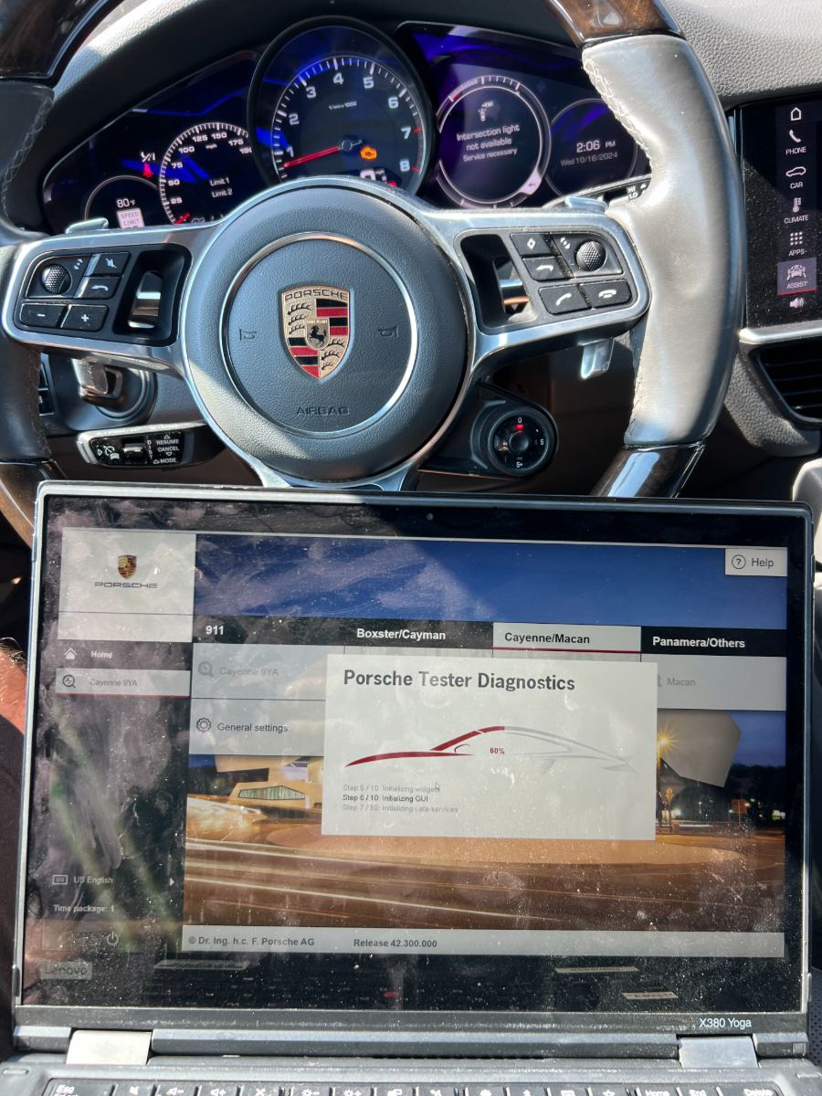 Porsche Cayenne steering wheel with Porsche Tester Diagnostics loading on a connected laptop showing 911, Boxster/Cayman, Cayenne/Macan and Panamera tabs